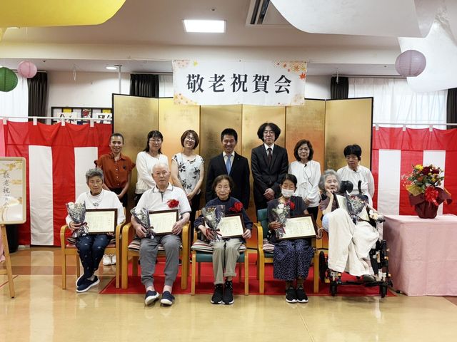 敬老祝賀会の参加者 多目的室 明るく彩られた空間で、敬老を祝う会が行われています。参加者の皆さんが笑顔で集合しています。