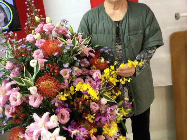 笑顔のスタッフと花<br> スタッフイメージ<br> 華やかな花束を手にしたスタッフが、明るい雰囲気を醸し出しています。施設での交流をイメージできます。