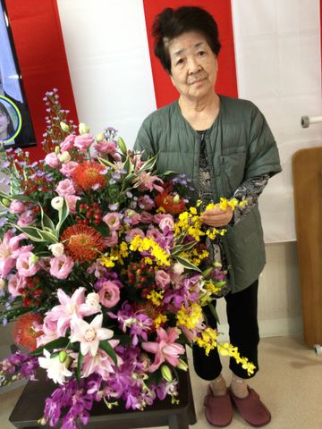笑顔のスタッフと花<br> スタッフイメージ<br> 華やかな花束を手にしたスタッフが、明るい雰囲気を醸し出しています。施設での交流をイメージできます。
