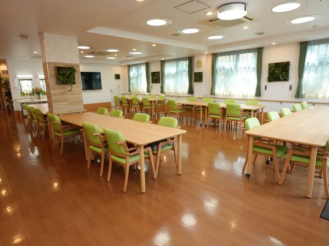 国旗飾り付けの食堂空間 共有スペース 広々とした食堂は、天井の高さと各国の国旗で国際的な雰囲気が感じられます。明るい日差しの中、利用者様は食事や交流を楽しんでいます。