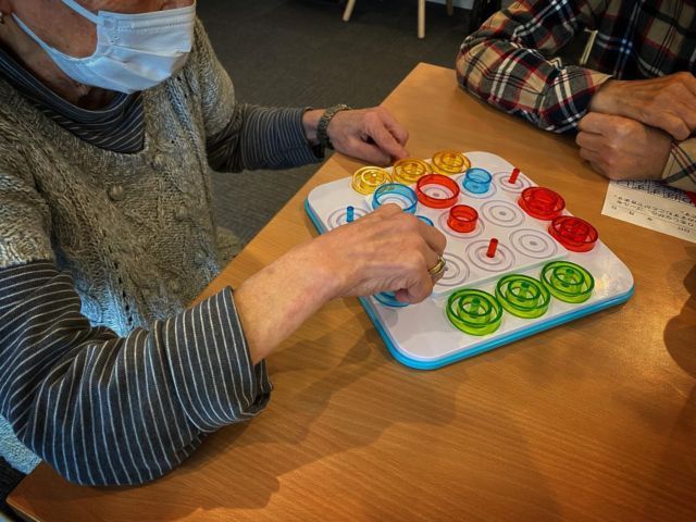 ゲームを楽しむ様子の共有スペース ラウンジ 施設のラウンジでは、入居者の方々が楽しくボードゲームに取り組んでいます。リラックスした空間です。