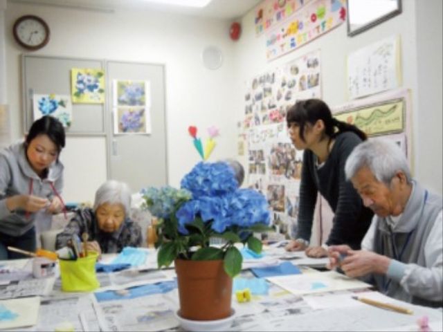 多目的室での手工芸活動 機能訓練 明るく清潔感のある空間で、スタッフのサポートのもと、入居者同士が楽しそうに創作活動を行っています。皆さんの表情からも温かい雰囲気が伝わってきます。