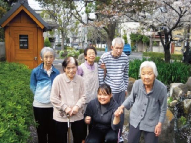 笑顔の人々と庭の風景 外出 緑豊かな庭では、利用者様が互いに交流を深め、穏やかなひとときを過ごしています。スタッフも一緒に笑顔で寄り添い、温かい雰囲気が感じられます。