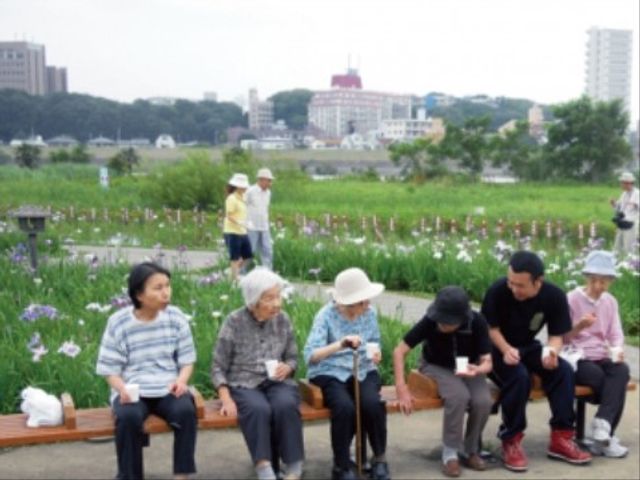中庭に集う人々 外出 広々とした中庭で、皆様が穏やかなひと時を過ごされています。自然に囲まれた環境で、日々のコミュニケーションをお楽しみいただける空間です。