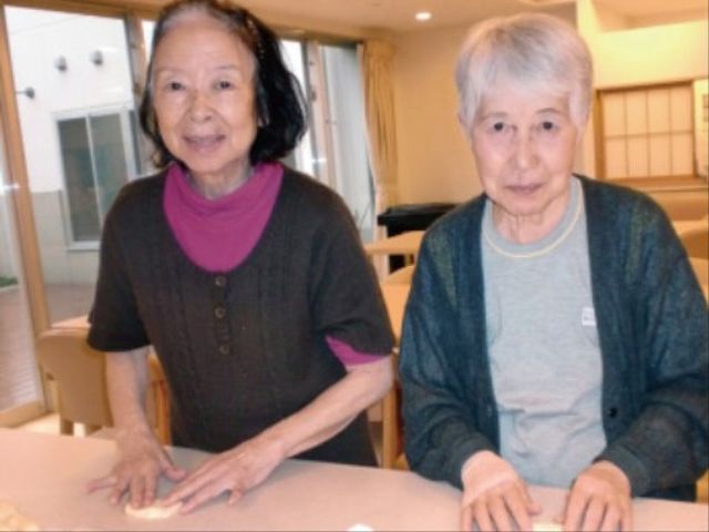 笑顔の高齢者二人とダイニング 食堂 居心地の良いダイニングで笑顔の高齢者が対話を楽しんでおり、職員としても温かな環境でのお仕事が期待できます。