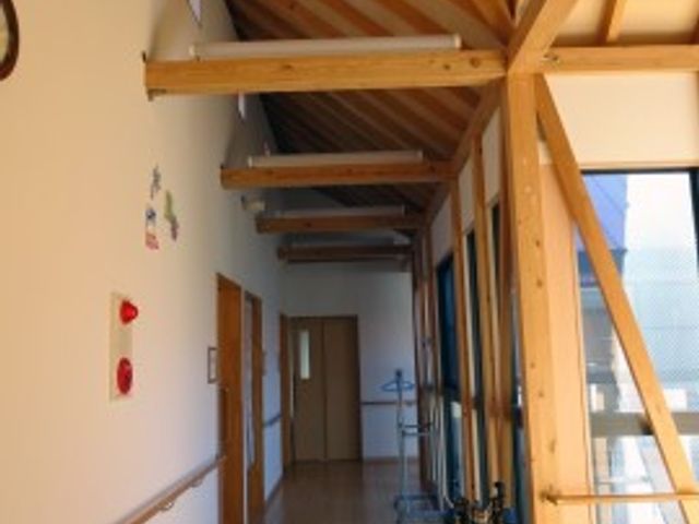 木造の明るい廊下空間 共用廊下 天井まで続く窓から自然光が差し込む廊下は、温かみのある木のぬくもりを感じさせてくれます。手すりが設置され、壁にはアートが飾られ、安心して歩ける落ち着いた雰囲気の空間です。