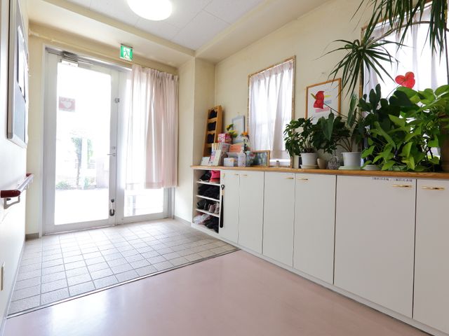 入口付近の明るい空間 エントランス(別カット) ゆとりあるエントランスは、自然光が差し込んでおり、素敵な観葉植物が迎えてくれます。利用者様の心地よい一日の始まりを支えます。