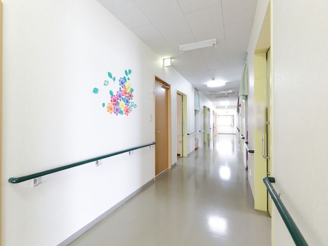 明るい廊下と装飾 共用廊下 手すり沿いに広がる廊下は清潔感があり、壁の花の装飾が暖かい雰囲気を醸し出しています。働く環境としても安心感があります。