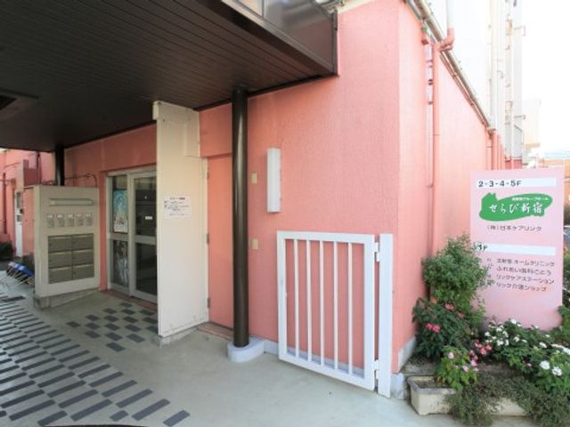ピンクの壁の建物入口 ケア 暖かみのあるピンク色の壁に囲まれた入口は、歓迎する雰囲気を醸し出しています。植栽が施されたスペースもあり、心地よい環境です。