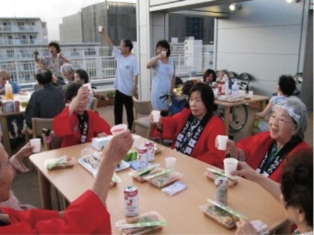 屋外での集いの様子 レクリエーション ゆったりとしたテラスでのコミュニケーションを大切にしており、笑顔で食事を楽しむ皆さんの姿が印象的です。