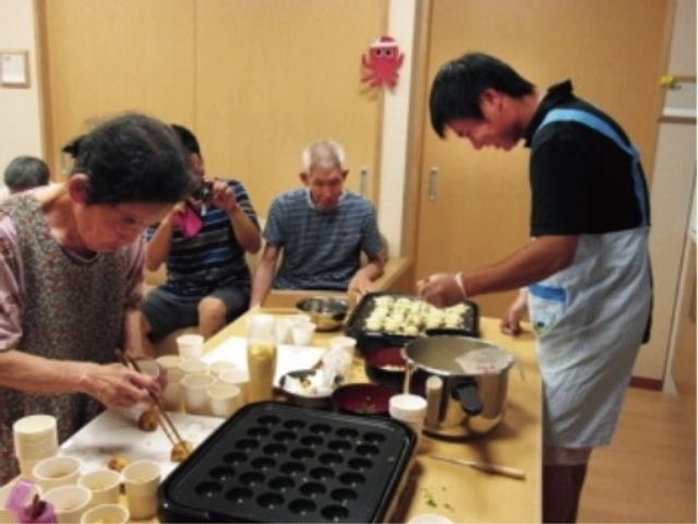 料理活動をする人々 レクリエーション 明るい雰囲気の食堂で、笑顔で調理をする方々が見受けられます。共に手料理を楽しむ時間は、穏やかなコミュニケーションが生まれる場となっています。
