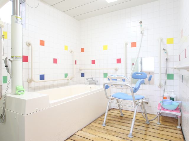 カラフルな浴室設備 個室バスルーム カラータイルが彩る清潔感のある空間です。利用者の安全を考えた手すりや椅子があります。