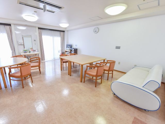 明るい食堂のスペース 談話室 ゆとりのある食堂には、天井が高く開放感があり、心地よい時を過ごすことができます。白いソファーや木製テーブルが配置され、温かみのある空間です。
