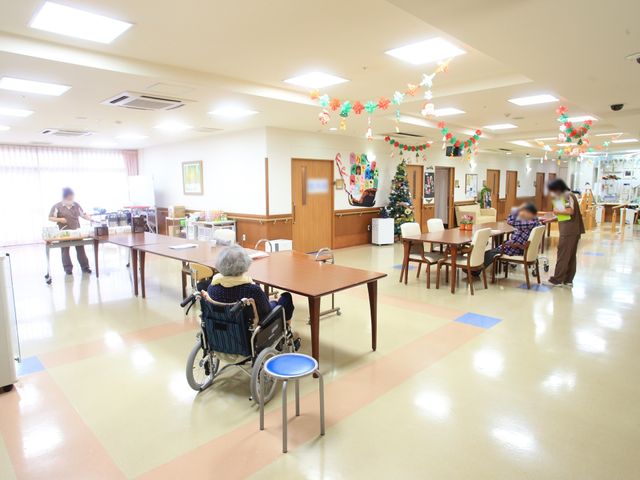 共有スペースの生活風景 食堂  明るく広々とした食事の場所です。職員と利用者が穏やかな時間を過ごしている様子がうかがえます。