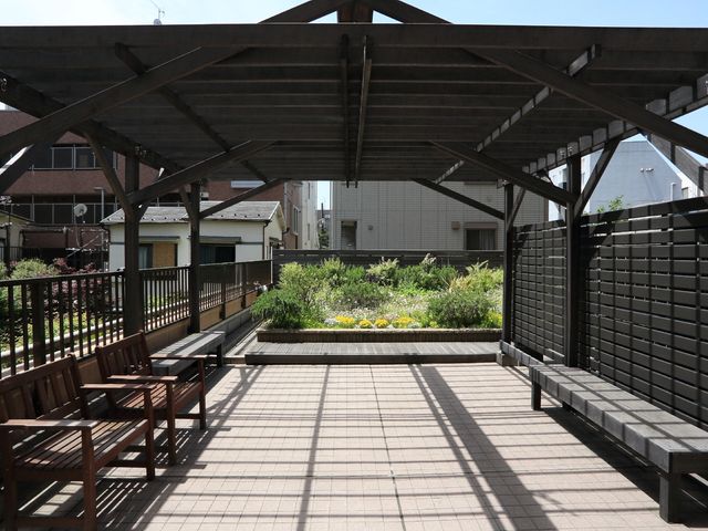 屋根付きの開放的な中庭 テラス 木製のベンチが並び、心地よい陽光が差し込む開放的な中庭です。自然の風を感じながら、ゆったりとした時間を過ごせる場所です。