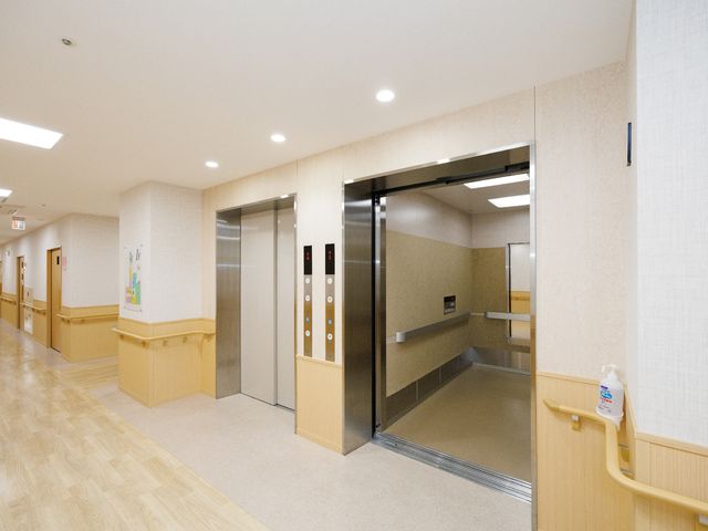 廊下にあるエレベーター エレベーター 清潔で明るい廊下のエレベーターは、スムーズな移動を支えております。手すりも設置しており、利用者さまの安全に配慮されています。