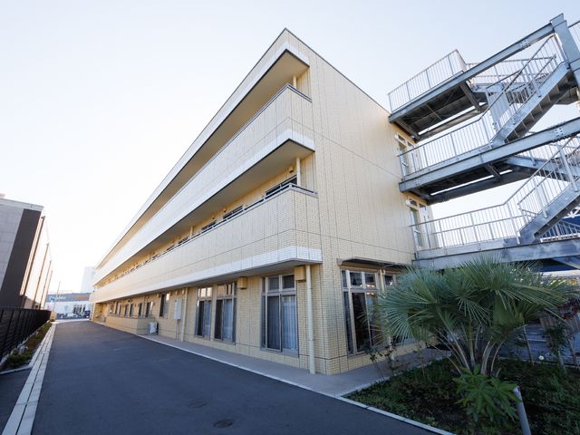 明るい施設の外観 外観 手入れの行き届いた緑と清潔感のある建物が迎えてくれる、やすらぎの場所です。明るい朝日が心地よく、新たな一日のスタートにふさわしい環境がここにあります。
