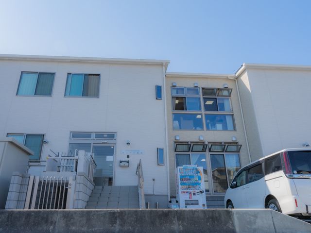 清潔な白い建物エントランス 外観 ゆったりとしたアプローチが特徴のエントランスです。訪れる方々を温かく迎え入れる設計となっておりますので、安心してご活動いただけます。
