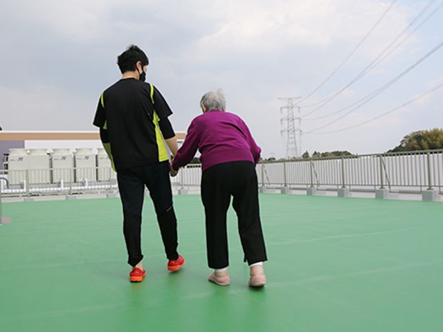 屋上で歩く様子 テラス 開放的なテラスで、スタッフが安全を見守りながら一緒に歩いています。