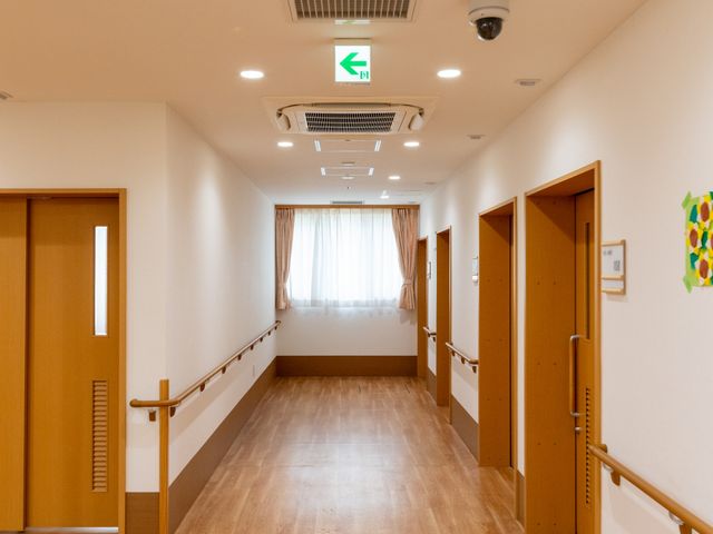明るい廊下 廊下   木目調の床と手すりがあり、移動しやすい廊下です。自然光も入り、落ち着いた雰囲気で働けそうです。