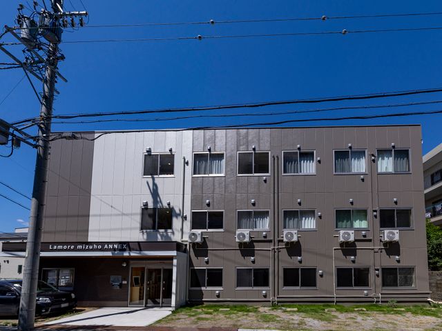 快適そうな建物の外観 外観 清潔感のある外壁と整った入口が、安心感を与える施設の顔です。空と緑に恵まれた周囲の環境も魅力的です。