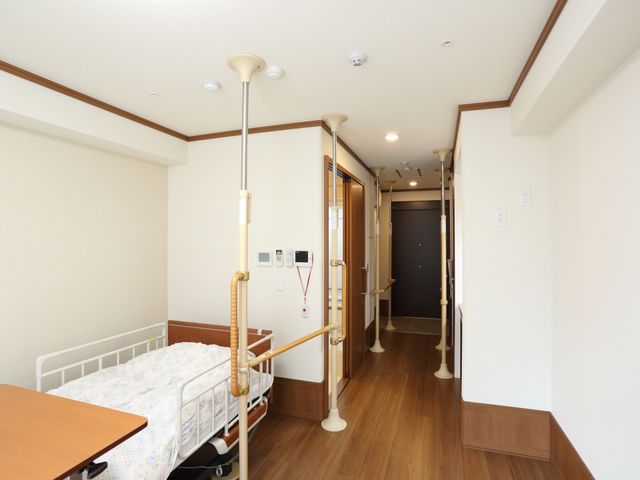手すり付きの廊下 居室 手すりが設置された廊下は、広々として明るく、利用者の移動をサポートします。安全な歩行のための配慮が見られる環境です。