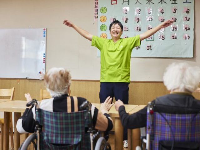 笑顔で体操をする様子 多目的室 笑顔溢れるスタッフの方が、楽しそうに体操の指導をされています。参加されている方々も元気に動かれています。