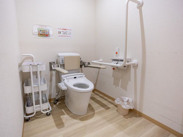 手すり付きのトイレ トイレ   手すりが複数あり、移乗や立ち座りを支えやすいトイレです。明るい壁とすっきりした床で、清潔感があります。