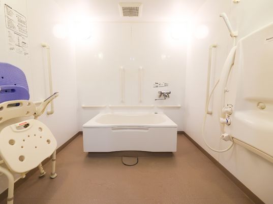 壁に手すりが配置された白い部屋の中央に置かれた浴室