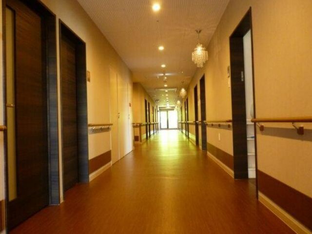 廊下の照明と手すり 廊下 ゆったりとした幅広い廊下が確保されており、壁には安全のための手すりが取り付けられています。清潔感があり、温かみのあるデザインです。