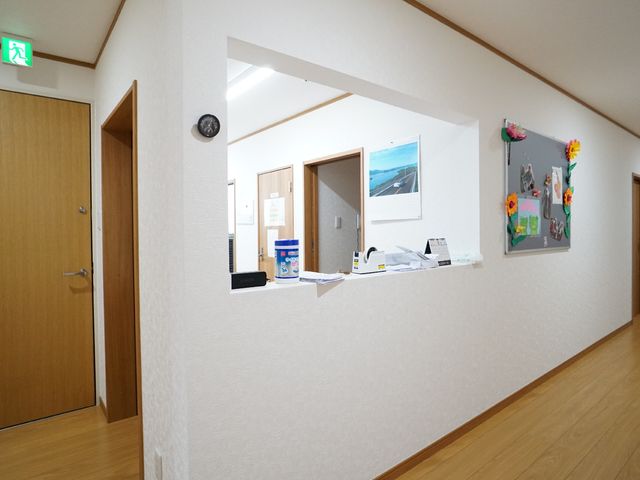 廊下と受付の様子 受付 清潔で明るい廊下が広がっており、受付も見渡せる設計です。壁に飾られた花や風景の絵が、暖かい雰囲気を醸し出しています。