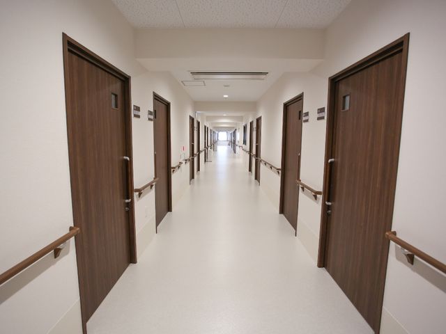 清潔な廊下の全景 廊下 床がピカピカに磨かれた廊下は、訪れる人々に安心感を与えます。手すりが整った長い通路は、ご利用者の移動を支えます。