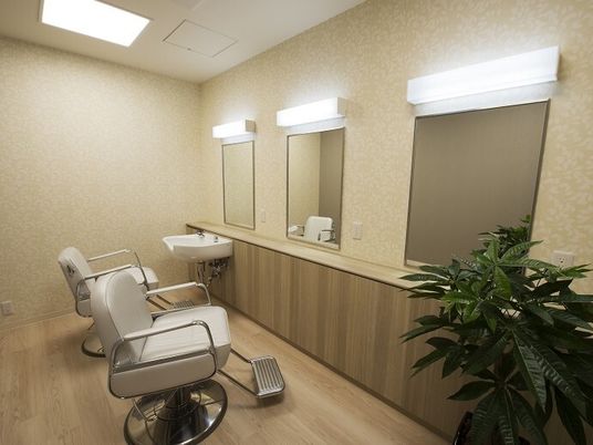 美容院で使用されている回転式の椅子が設置されたスペース。壁には鏡があり、奥には洗髪台がある。