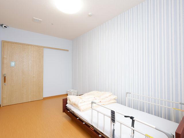 洋室のベッドとドア 居室 明るく落ち着いた雰囲気の個室です。手すり付きのベッドで安全にお過ごしいただけます。