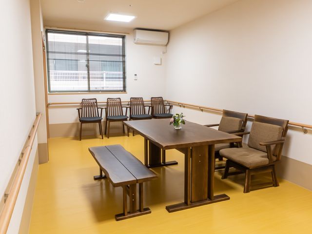 多目的スペースの明るい部屋 共有スペース 落ち着いた色合いの家具が並ぶ快適な空間で、コミュニケーションや憩いの場として利用できます。窓からは自然光が差し込み、日中でも明るい雰囲気が広がっています。