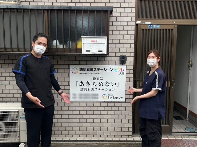 看板前のスタッフ 看板 笑顔のスタッフが歓迎している屋外のスペースです。安心感のある温かい雰囲気が伝わってきます。
