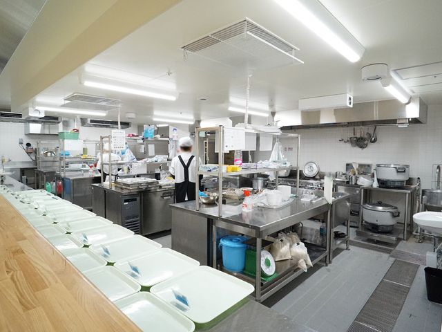 厨房作業中の職員 共有スペース 清潔で整理されたキッチンで、職員が食事の準備に勤しんでいます。栄養バランスに配慮した食事は、利用者に喜ばれる重要なポイントです。