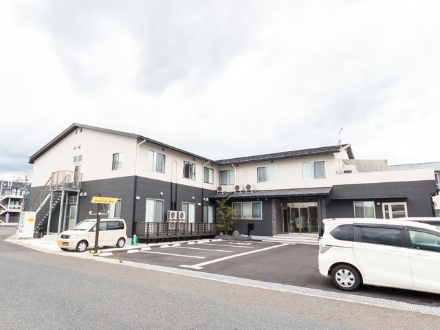 灰色の外壁の建物エントランス 外観 広々とした駐車場が完備されたモダンな建物の入り口です。来訪者を温かく迎える設計になっております。