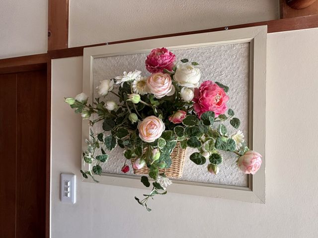 壁に飾られた花のアレンジメント 装飾 壁面に優しい色合いの花を配したアレンジメントがあり、居心地の良い空間作りに一役買っています。