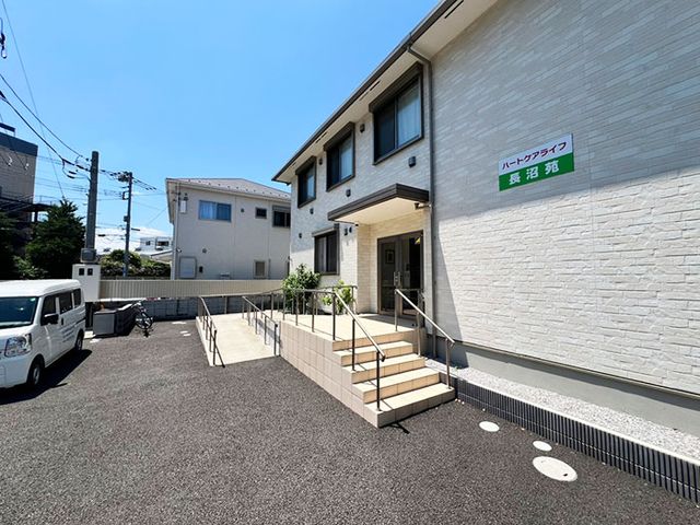 白い建物のエントランス エントランス 広々としたエントランスには、スロープ付きの階段があり、車椅子でのアクセスも便利です。