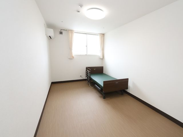 居室のベッドと窓 居室 清潔感あふれる居室で、窓からは光が差し込みます。個人のスペースを大切にしながら、安心して日々を送れる環境です。