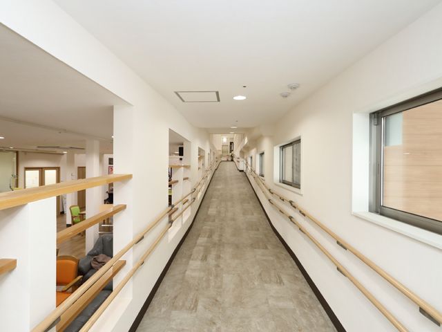 明るい施設の廊下 スロープ 手すりが設けられたゆったりとした廊下です。窓から自然光が差し込み、心地よい環境で働けます。