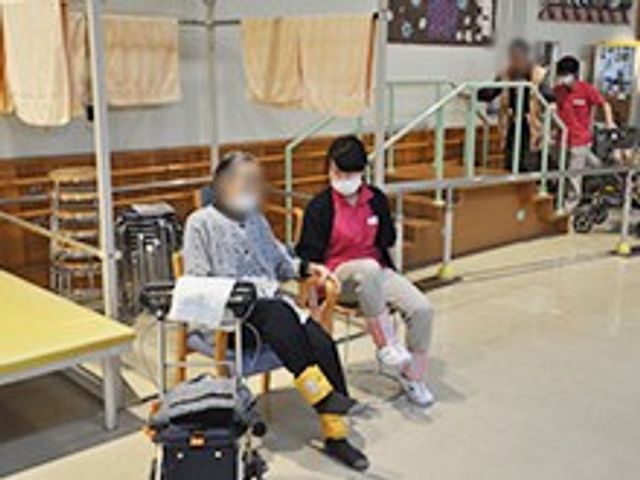機能訓練中の様子 機能訓練室 利用者の方が職員と一緒に軽い運動を行う様子です。親しみやすい雰囲気が感じられます。
