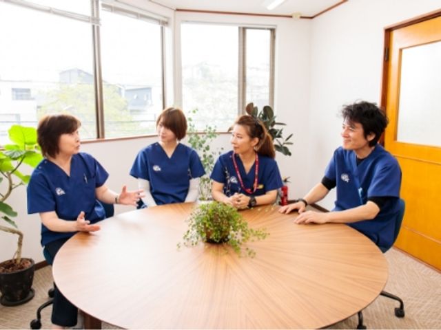 スタッフが会話する室内 スタッフイメージ 明るい室内でスタッフが会話を楽しんでいます。和やかな雰囲気の職場環境が特徴です。