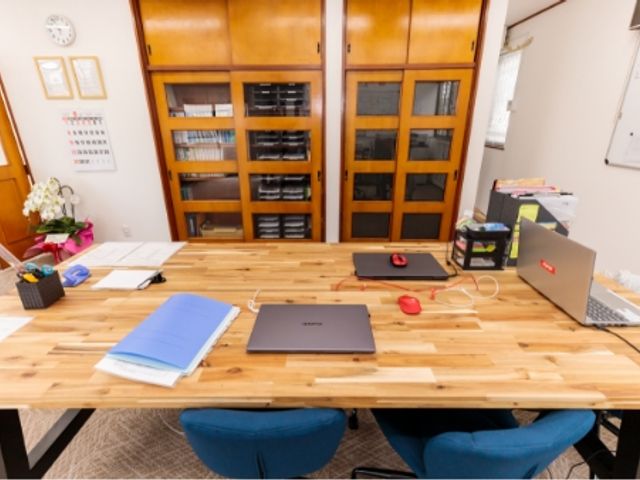 資料が並ぶ部屋の机 内観 広々としたデスクには作業用のノートパソコンが並んでおり、落ち着いた雰囲気があります。