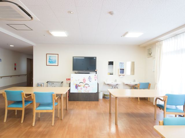 広々とした明るい食堂 共有スペース 床から天井まで光が射し込む明るいダイニングで、テレビを視聴しながら心地よい食事時間を過ごせます。余裕を持ったテーブル配置はご高齢者にも配慮されています。