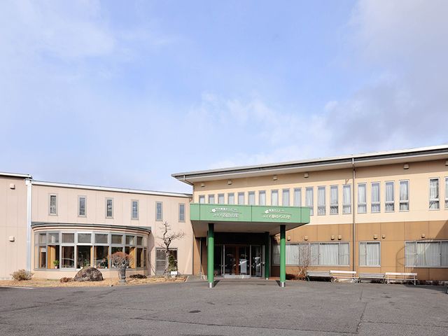 緑の屋根とベンチの庭 外観 ゆったりとした中庭にはベンチが配置され、介護施設の明るい入口が印象的です。