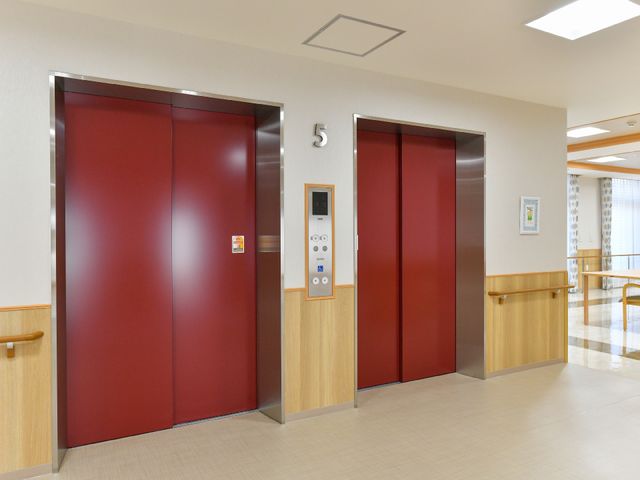 赤いエレベーターのドア エレベーター 木目と赤色のエレベーターは広々としており、フロアの移動が快適に行えます。周囲は清潔で明るい印象を与える造りです。