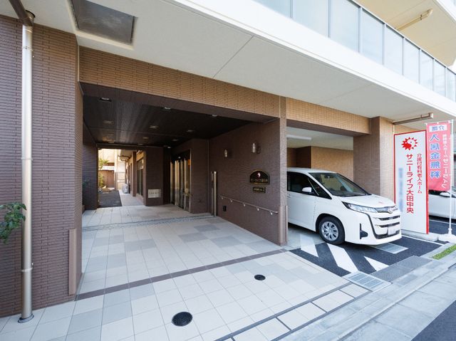 エントランスの様子 玄関 広々としたエントランスは、来訪者を明るく迎え入れます。通りからのアクセスも良好で、白い車が停まっており安心感があります。