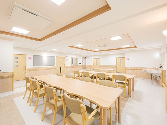 清潔な施設の食堂 共有スペース 広々とした食堂には木製のテーブルと椅子が並び、ゆったりと食事を楽しめる空間が広がっています。調和の取れた明るい色彩が、心地よいひと時を約束します。